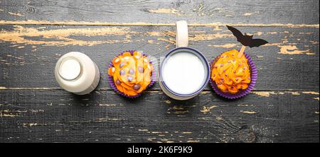 Leckere Halloween Cupcakes und Milch auf schwarzem Holzhintergrund, Draufsicht Stockfoto