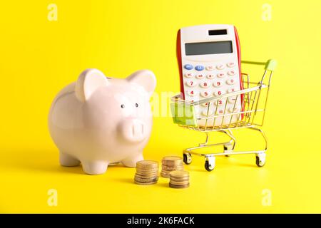 Sparschwein, Geld und Warenkorb mit Rechner auf farbigem Hintergrund Stockfoto