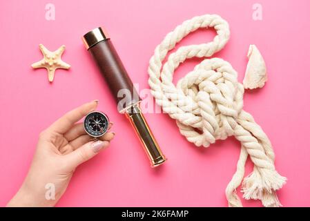 Weibliche Hand mit Kompass, Spyglass, Seil und Seestern auf farbigem Hintergrund Stockfoto