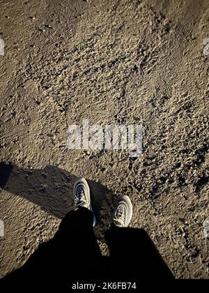 Eine vertikale Aufnahme einer Person, die ihre Füße mit Schatten auf dem Boden fotografiert Stockfoto