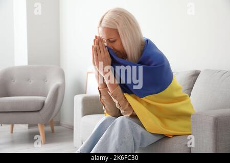 Reife Frau mit Fahne der Ukraine zu Hause beten Stockfoto