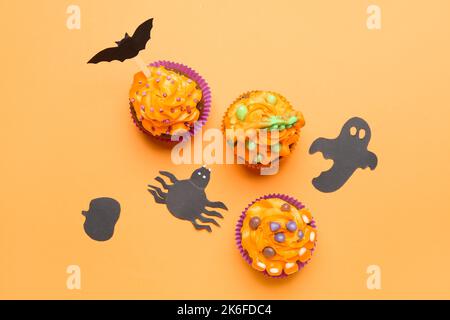 Leckere Halloween Cupcakes mit Papierdekor auf orangefarbenem Hintergrund Stockfoto