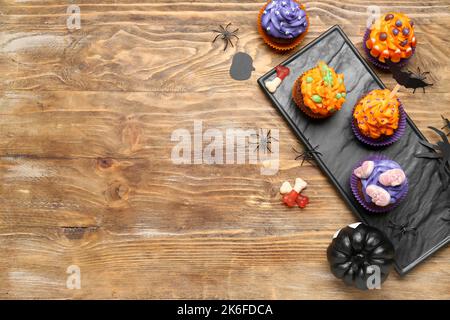 Brett mit Halloween Cupcakes, Bonbons und Spinnen auf Holzhintergrund Stockfoto