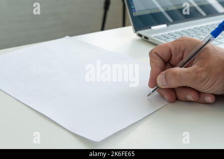 Eine Hand mit einem Stift in Nahaufnahme kennzeichnet ein leeres Papierdokument. Ein Mann füllt eine weiße, leere Papierform mit einem Stift aus der Nähe in hellem Sonnenlicht. Stockfoto