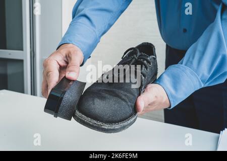 Der Mann wischt die Schuhe mit einem speziellen, eingeweichten Schwamm ab. Tanzschuhe putzen, schwarz Stockfoto