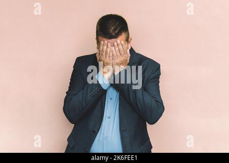 Stilvoller Geschäftsmann bedeckt sein Gesicht, seinen Bürostil. Handfläche mit Schilder. Ein Mann in einer blauen Jacke hält deutlich einen schmerzenden Kopf. Müdigkeit bei der Arbeit ist ein Koncep Stockfoto