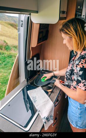 Frau trocknet pa im Wohnmobil, während Mann Ukulele im Freien spielt Stockfoto