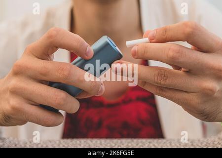 Raucher rauchen Hybrid rauchlose Zigarettengerät, das echte Tabak Nachfüllungen verwendet, Hybrid-Technologie zwischen analogen und elektronischen Zigaretten. Mann füllt Stockfoto