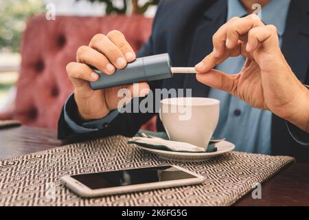 Raucher rauchen Hybrid rauchlose Zigarettengerät, das echte Tabak Nachfüllungen verwendet, Hybrid-Technologie zwischen analogen und elektronischen Zigaretten. Mann füllt Stockfoto