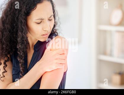 Stress kommt in vielerlei Hinsicht auf. Eine junge Geschäftsfrau, die ihre Schulter vor Schmerzen am Arbeitsplatz hält. Stockfoto