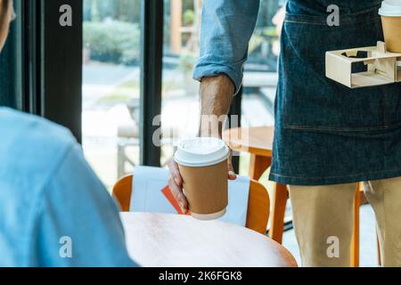 asiatisches Personal mit Schürze, das den Gästen auf dem Tisch im Café-Café, Café-Restaurant, Inhaber eines kleinen Unternehmens, Service-Geist, heiße schwarze Kaffeetasse serviert Stockfoto