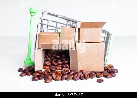 Umgestürzter Miniatur-Einkaufswagen mit winzigen Kartons mit gerösteten Kaffeebohnen auf weißem Hintergrund. Store Delivery Konzept. Stockfoto