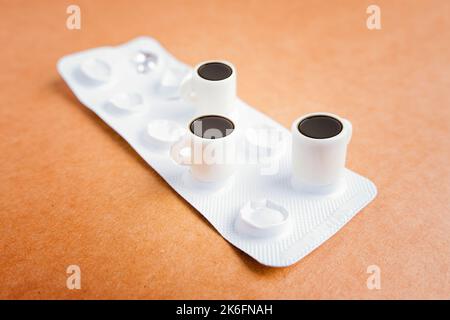 Mini-Kaffeetassen auf einer Tablette Blister isoliert platziert. Koffein als Schmerzmittel. Stockfoto