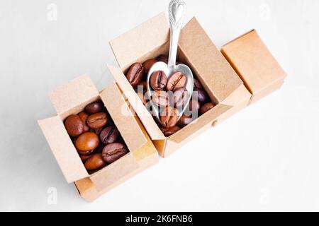 Nehmen geröstete Kaffeebohnen mit einem kleinen Teelöffel aus Miniatur-Kartons isoliert auf weißem Hintergrund. Coffee Shop liefert Konzept. Stockfoto