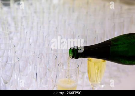 Nahaufnahme einer Champagnerflasche, die Champagner in eine Sektflöte vor einem verschwommenen Glas im Hintergrund pochelt Stockfoto