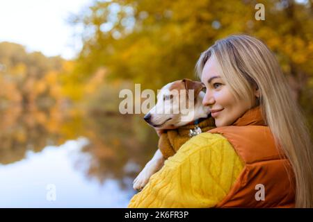 Porträt einer lächelnden jungen Frau, die einen Hund auf einem Feld küsst. Hundeliebhaber stilvolles Mädchen umarmt ihren Hund beim Gehen. Konzept der Tierfreundschaft Stockfoto