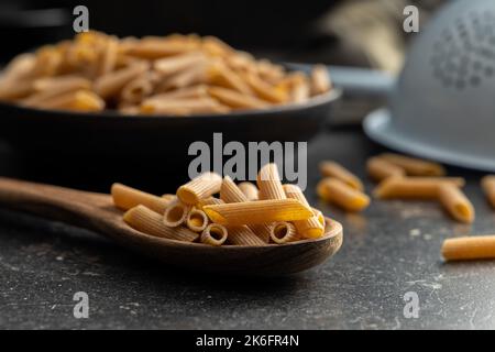 Ungekochte Vollkornpasta. Rohe Penne Pasta auf dem Holzlöffel. Stockfoto