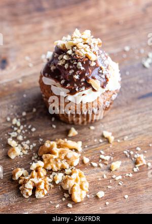 Leckerer Schokoladenmuffin mit Creme Mascarpone und Schokolade darüber, mit Nüssen überzogen. Auf Holztisch platziert. Süßer, frischer und hausgemachter Cupcake. Stockfoto