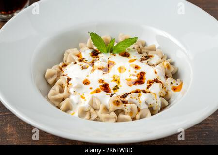 Kayseri ravioli oder Kayseri Mantisi auf einem weißen Teller auf einem Holztisch Stockfoto