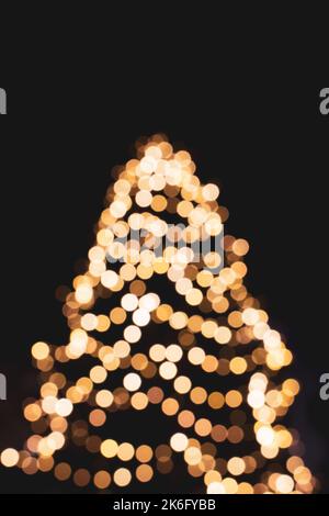 Goldener Weihnachtsbaum, unfokussiert. Beleuchteter weihnachtsbaum auf schwarzem Hintergrund, Bokeh. Leuchtende Lichter. Weihnachtsfeier. Winterurlaub. Stockfoto