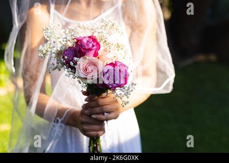 Eine afroamerikanerin, die ein Hochzeitskleid trägt und am Hochzeitstag Blumen in der Hand hat Stockfoto
