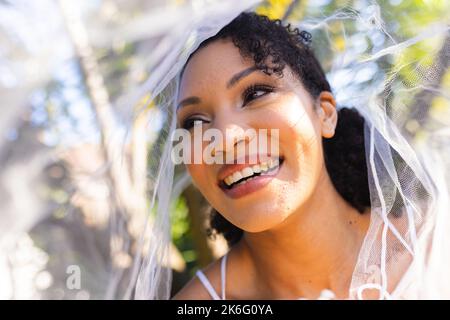 Eine glückliche afroamerikanische Frau, die am Hochzeitstag Hochzeitskleid und Schleier trägt Stockfoto
