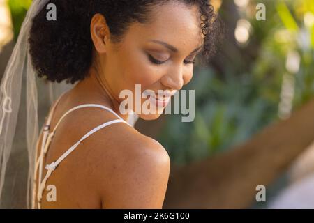 Eine glückliche afroamerikanische Frau, die am Hochzeitstag Hochzeitskleid und Schleier trägt Stockfoto