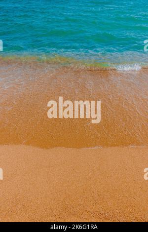 Vertikales Foto von kristallklarem Wasser im Ozean und kleinen Wellen am Sandstrand, Spanien Stockfoto