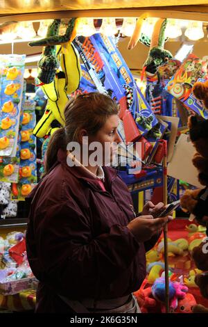 7.. Oktober 2022, Tewkesbury, Gloucestershire, England. Tewkesbury Mop Fair. Die Mitarbeiter am Telefon, während sie auf der Tewkesbury Mop Fair auf die Kunden warteten. Die Tewkesbury Mop Fair findet seit 1199 statt und ist eine der größten und bekanntesten traditionellen Straßenmessen des Landes. Stockfoto