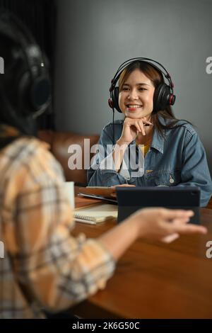 Aufnahme einer lächelnden jungen Radiomoderatorin, die während der Podcast-Aufnahme im Heimstudio interessante Gespräche mit Gästen hört Stockfoto