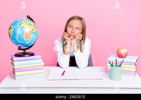 Foto von jungen lustig ziemlich niedlich Schulkind Mädchen tragen einheitliche sitzen Schreibtisch Kurse gelangweilt gesinnten Touch Kinn suchen leeren Raum isoliert auf rosa Farbe Stockfoto