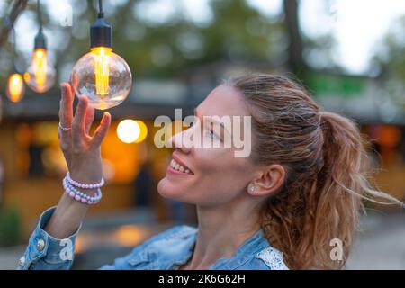 Junge kaukasische Frau hält energieeffiziente LED-String-Glühbirne im Freien Stockfoto