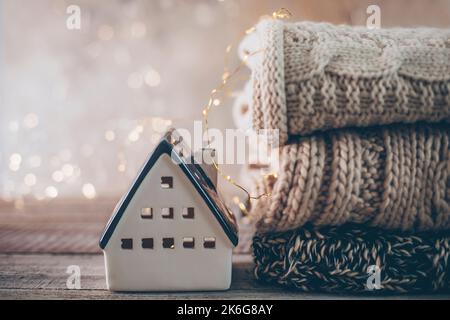 Stapel von gemütlichen Winter-Strickpullover, Keramikhaus auf einem verschwommenen Hintergrund mit Bokeh. Warmes, Gemütliches Konzept. Stockfoto