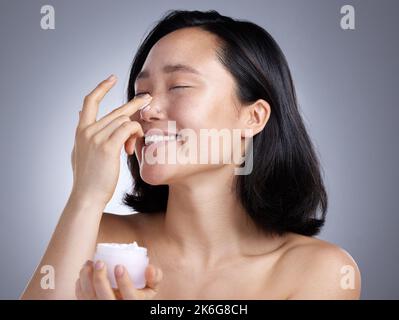 Meine Haut liebt das. Eine junge Frau, die Lotion auf einem grauen Hintergrund auflegt. Stockfoto