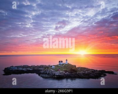 Nubble Lighthouse Aerial Sunrise - Luftaufnahme eines wunderschönen, dramatischen Himmels mit der aufgehenden Sonne hinter dem ikonischen Nubble Light am Cape N Stockfoto