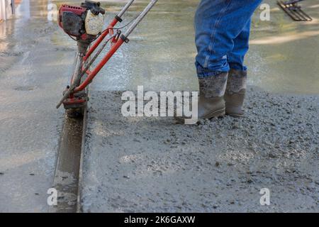 Es ist notwendig, eine Maschine zu verwenden, um die frisch verdichtete Betonschicht auf der neuen Auffahrtkonstruktion auszurichten Stockfoto