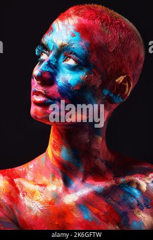 Farbe ist nur Poesie auf Leinwand. Eine attraktive junge Frau, die allein im Studio posiert und Farbe auf Gesicht und Körper hat. Stockfoto