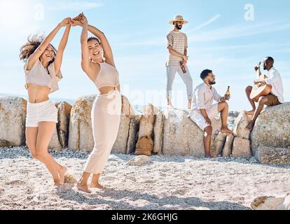 Ihre glücklichen Herzen durch Tanz auszudrücken. Zwei junge Frauen tanzen am Strand mit ihren Freunden. Stockfoto