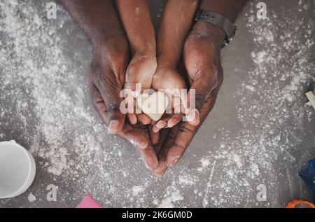 Cookies sind das süßeste kleine Stück von Komfort-Essen. Ein unbekanntes Mädchen und ihr Vater halten zu Hause in der Küche einen herzförmigen Keks. Stockfoto