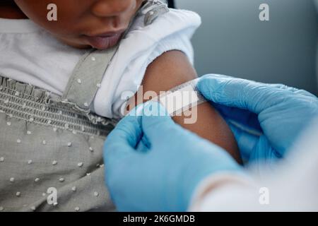 Dadurch fühlen Sie sich bald besser. Nahaufnahme eines nicht erkennbaren Arztes, der nach einer Injektion einen Pflaster auf einen kleinen Mädchenarm aufgibt. Stockfoto