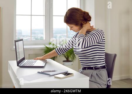 Müde, gestresste Frau mit Schmerzen im Nacken, die am Schreibtisch am Laptop arbeitete Stockfoto