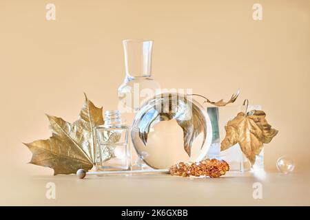 Biophiler Herbsthintergrund. Vergoldete Ahornblätter aus Gold, verzerrt durch transparente Glasgläser, kleine Flaschen. Einfarbig orange beige florale Elemente Stockfoto