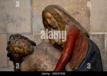 Die trauernde Jungfrau Maria, dargestellt mit langen goldenen Haaren, starrt Christus ins Gesicht, während sie nach der Kreuzigung seinen Körper hält. Detail der flämischen burgundischen Pietà Ende 1400s in der Cathédrale Saint-Cyr-et-Sainte-Julitte in Nevers, Bourgogne-Franche-Comté, Frankreich. Die mehrfarbigen Kalksteinarbeiten spiegeln den Stil von Claus Sluter wider, Hofbildhauer des Herzogs von Burgund aus dem Jahr 1380s. Stockfoto