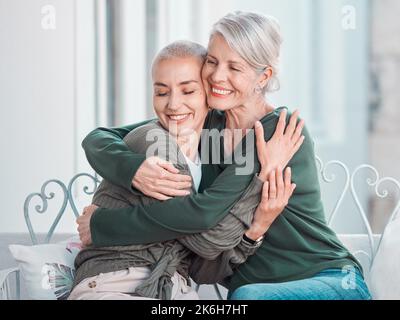 Fröhliche ältere Mutter umarmte Erwachsene Tochter. Liebende kaukasische Mutter umarmte ihre Tochter, während sie zu Hause zusammen saß. Ältere Frau sieht glücklich aus Stockfoto
