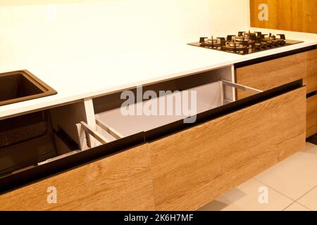 Moderne Küchenschränke aus braunem Holz, stilvolle schwarze Granitwaschbecken und Gasherd aus Glas in einem Haus, offene Schubladen Stockfoto