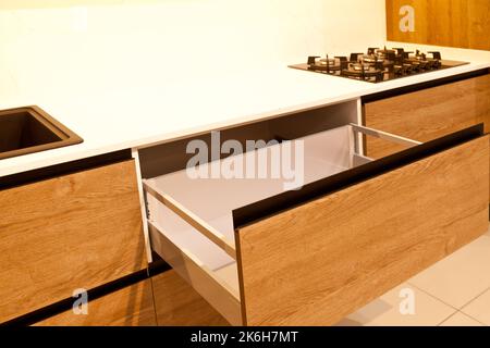 Moderne Küchenschränke aus braunem Holz, stilvolle schwarze Granitwaschbecken und Gasherd aus Glas in einem Haus, offene Schubladen Stockfoto