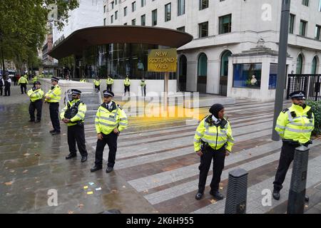 Polizeibeamte umgeben ein Schild, das von einem Protestierenden von Just Stop Oil vor dem New Scotland Yard in London mit Sprühnebel bemalt wurde. Bilddatum: Freitag, 14. Oktober 2022. Stockfoto