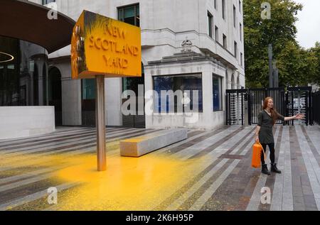 Ein „Just Stop Oil“-Protestler steht neben einem Schild, das sie vor dem New Scotland Yard in London besprüht hat. Bilddatum: Freitag, 14. Oktober 2022. Stockfoto