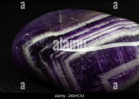 Echtes gestrommenes purpurnes und weißes Chevron-Amethyst, das auf das Makro der schwarzen Oberfläche fokussiert ist Stockfoto