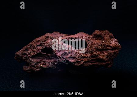 Roter rauer echter Lavastein Makro fokussiert und isoliert auf schwarzer Oberfläche isoliert Stockfoto